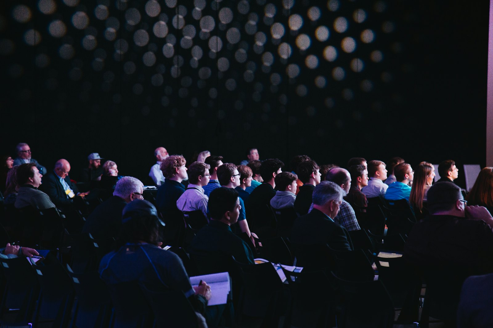 A conference audience seated in a dark hall — the kind of venue where mobile signal disappears
